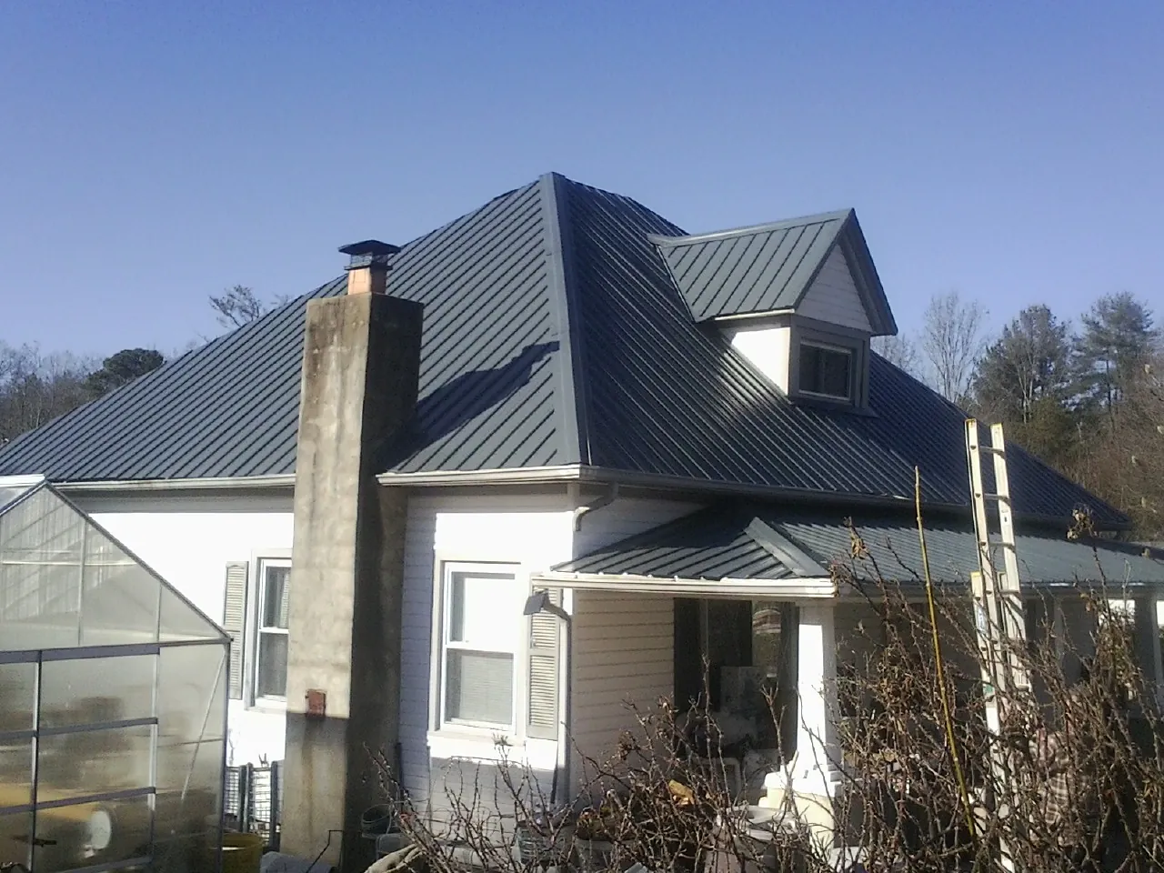 Dark blue standing seam metal roof on a white farmhouse with dormer — Slate & Tile Roof Repair by Roofing Brothers in Ridgewood