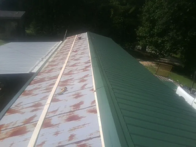 Old rusted panels beside newly installed green metal roofing — Wind Damage Roof Repair by Roofing Brothers in Ridgewood
