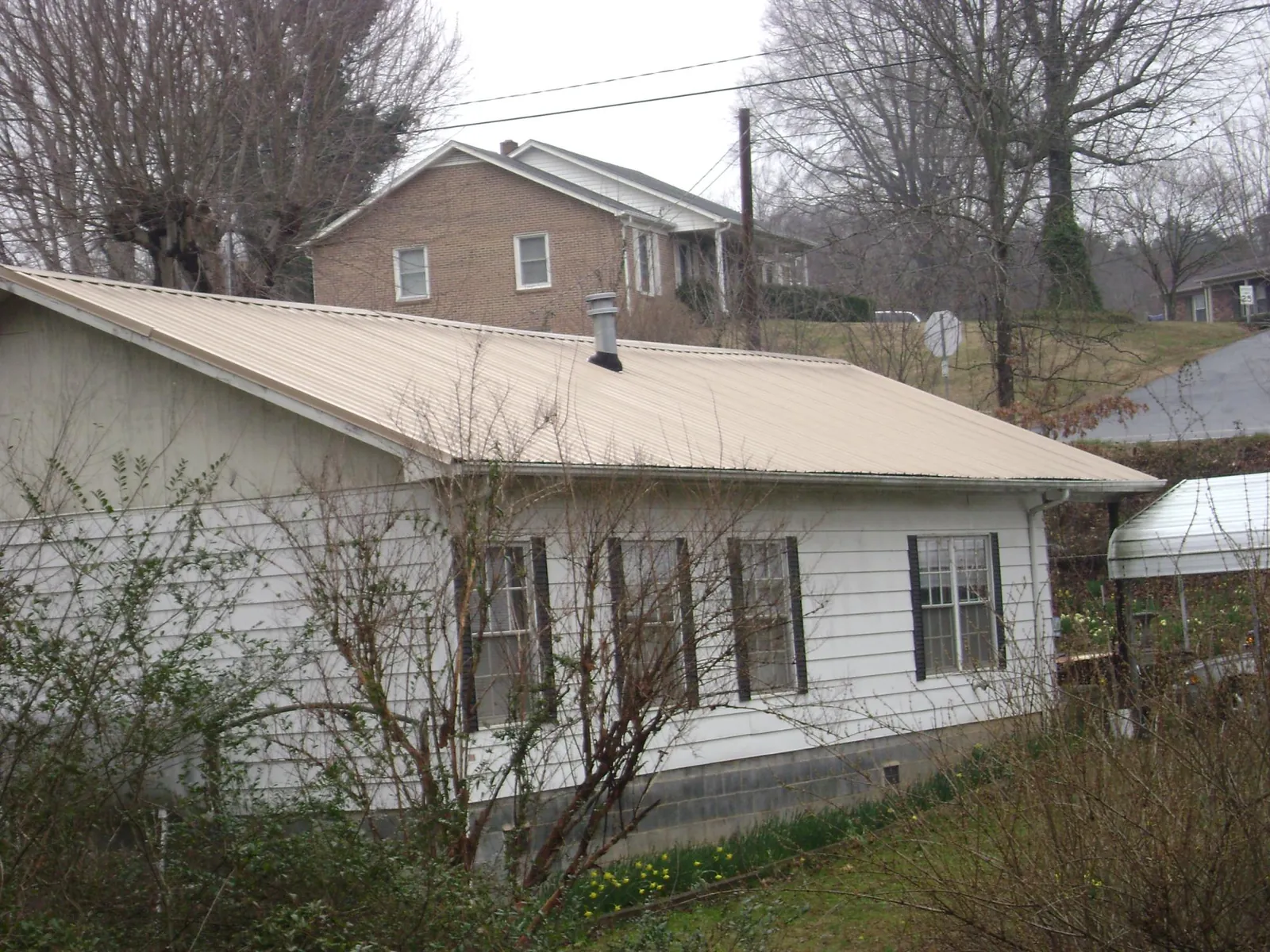 Tan metal roof on a white sided house set into a hillside — Commercial Roofing by Roofing Brothers in Ridgewood